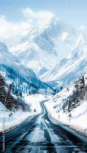 A winding mountain road cuts through a snowy landscape with tall pine trees and imposing snow-covered peaks under a blue sky.