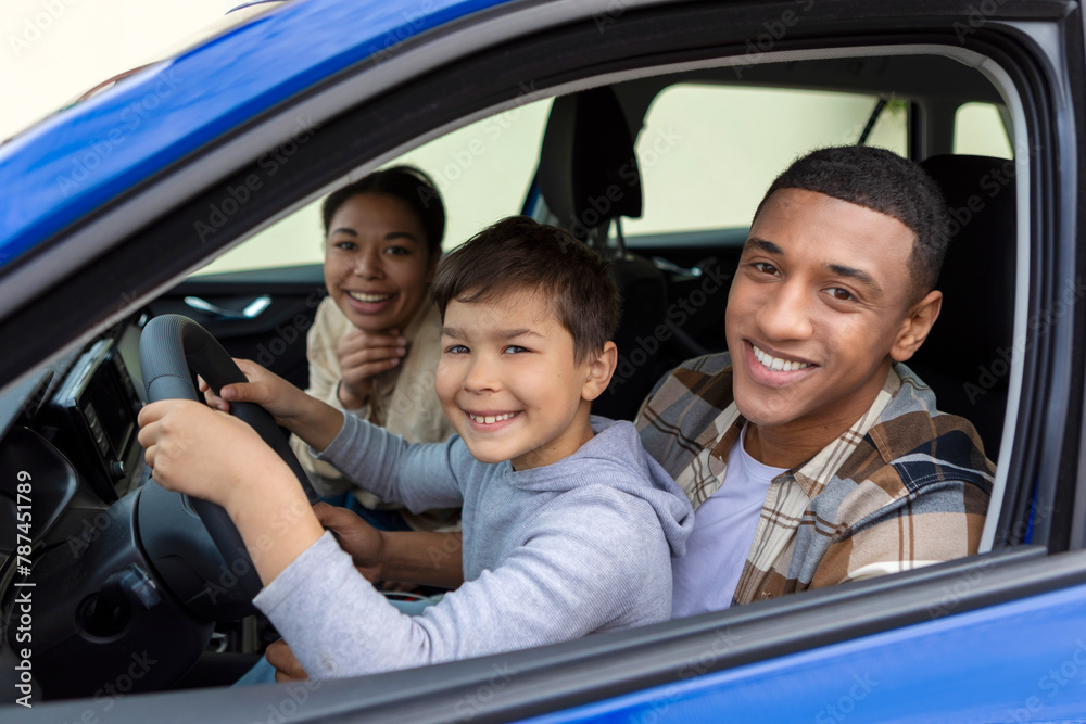 Happy preteen boy driving car, sitting with father in driver's seat smiling to camera, dad teaching son to drive Happy preteen boy driving car, sitting with father in driver's seat smiling to camera, dad teaching son to drive