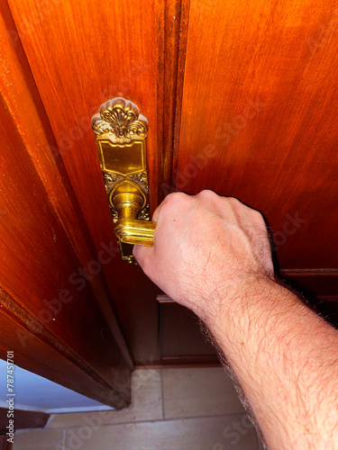 A hand is captured in the act of grasping a vintage golden door handle, ready to open a door. UGC.