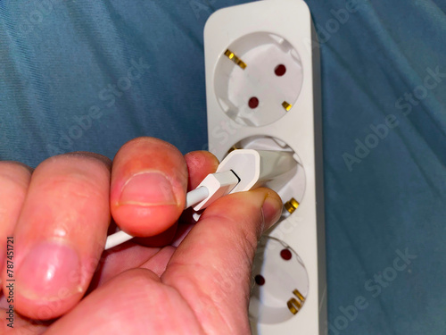 A hand skillfully connects a white charger to a multi-socket extension cord. UGC. 