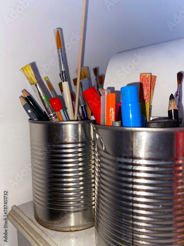 A collection of paintbrushes and pencils, each with their own story to tell, haphazardly organized in repurposed metal cans. UGC.