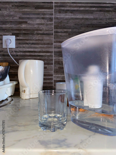 A clear glass and a water filter pitcher rest on a marble kitchen countertop, bathed in soft, natural light. This image encapsulates the simplicity of home hydration. UGC.
