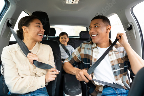 Joyful family of three riding new car, man and woman putting on seat belts for safety. Transportation, new auto concept photo