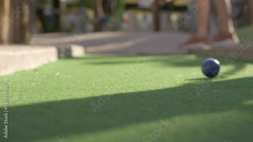 This video shows a mini golf ball being hit by a player and rolling towards the camera on the putting green. 