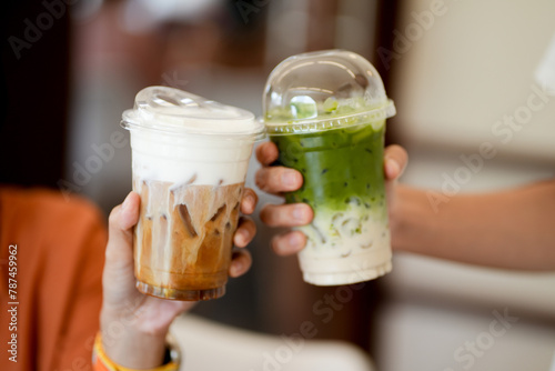 Close up and selective focus glass of ice coffee and ice matcha green tea on hands of teenage girls, drinking together at cafe.