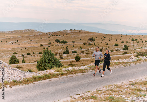 A couple dressed in sportswear runs along a scenic road during an early morning workout, enjoying the fresh air and maintaining a healthy lifestyle © .shock