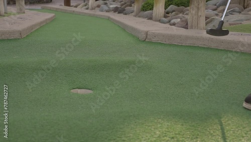 This video shows a slow motion side view of a red golf ball being putted into a miniature golf course hole.
