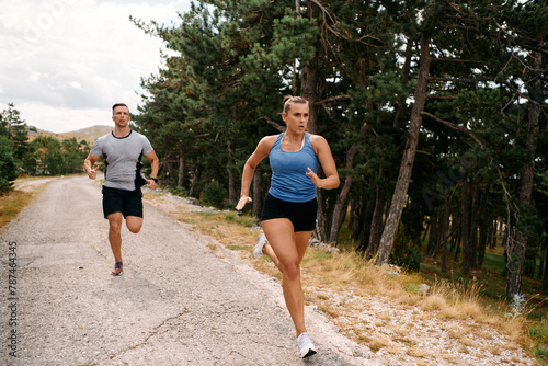 A couple dressed in sportswear runs along a scenic road during an early morning workout, enjoying the fresh air and maintaining a healthy lifestyle