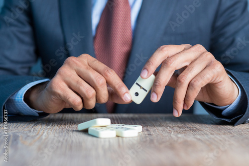 Business man stoping domino effect by his hand, business strategy background image, wearing blue suit and red tie photo