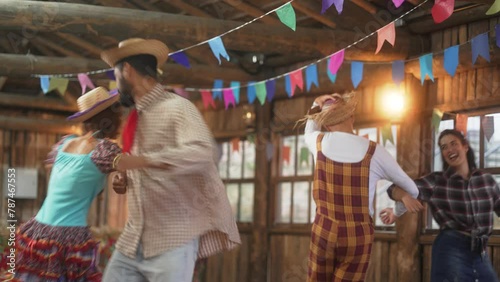 Couples Engaging in Square Dancing at Joyful Festa Junina Celebration. Revelers in Traditional Brazilian Costumes Twirling in a Rustic Barn Setting photo