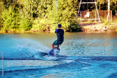 Fototapeta Naklejka Na Ścianę i Meble -  A man wakeboarding on a lake on summer day in a life  jacket. Soft focus. Action blur.