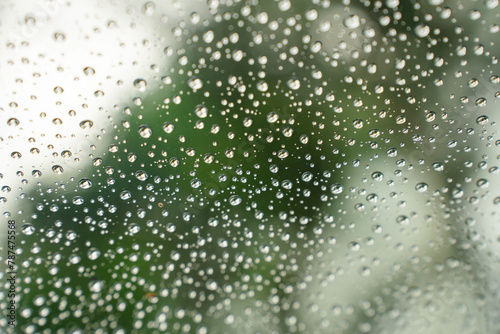 Water droplets on a clear glass surface, with a background of sky and blurred greenery.