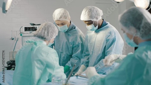 Group of mixed-races professional surgeons and nurses in uniform performing heart transplant surgery operation under bright lamps using medical instruments in operating room photo