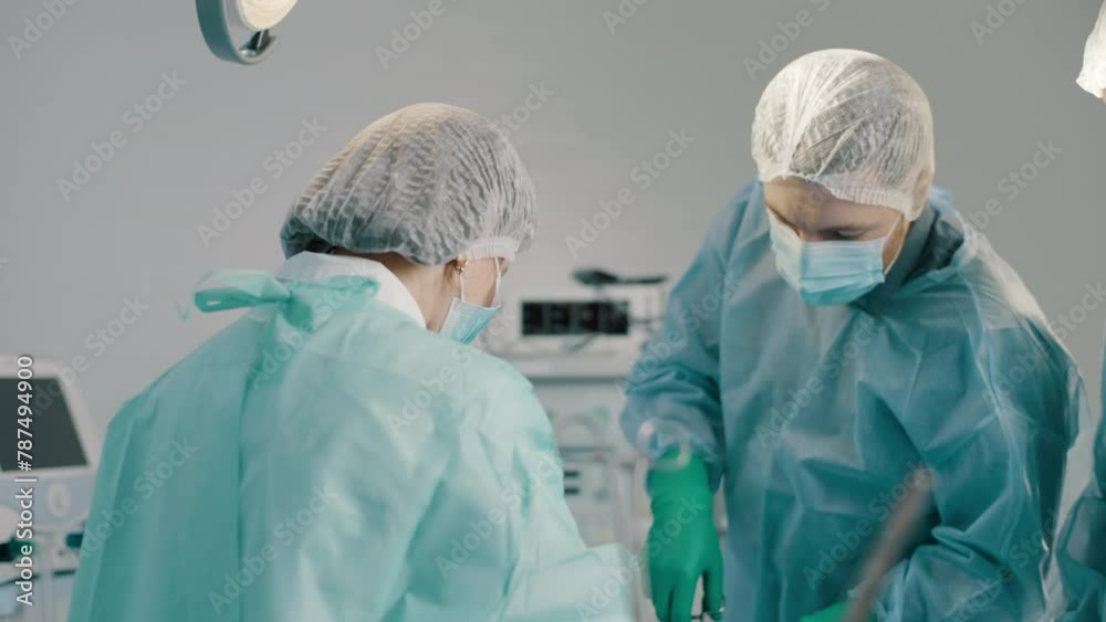 Team of professional surgeons performs surgery on patient under anesthesia in operating room. A nurse hands a medical instrument to a doctor Team of professional surgeons performs surgery on patient under anesthesia in operating room. A nurse hands a medical instrument to a doctor