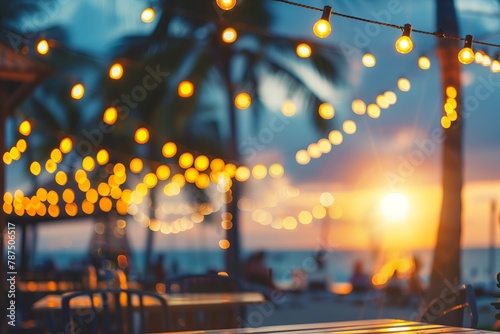blurred bokeh light on sunset with yellow string lights decor in beach restaurant.