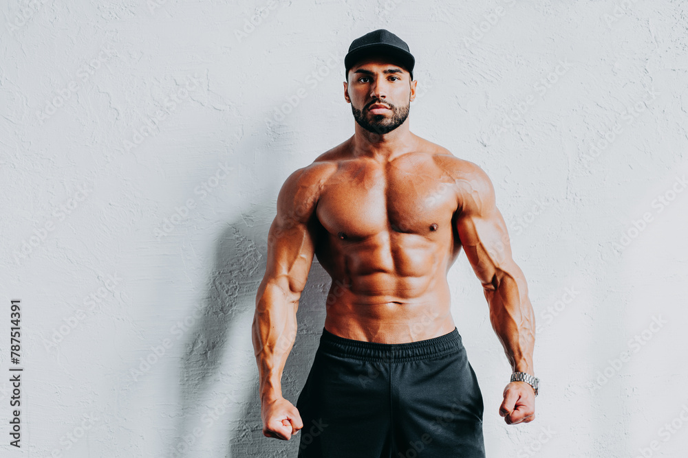Fototapeta premium Young strong man bodybuilder in cap on white wall background