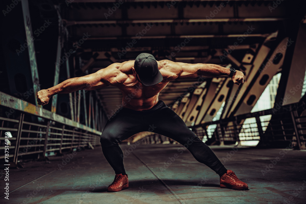 Fototapeta premium Young strong man bodybuilder posing on urban industrial background