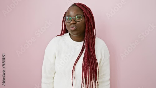 Adult black woman with braids wearing glasses and a white sweater, puckering lips over a pink wall background.