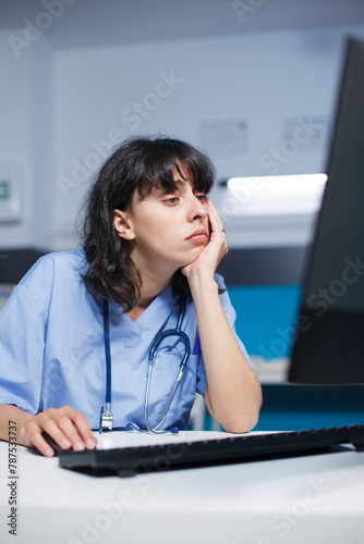 Caucasian female practitioner at a modern clinic desk, tired but focused. Before an appointment, pharmacist trained nurse analyzes a medical checkup using computer in the hospital office.