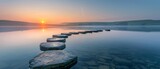 A serene sunrise casting warm light over a calm lake with stepping stones leading across the water.