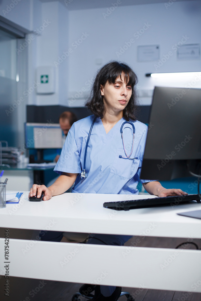 In clinic office, committed doctor using computer to analyze patient records. Female nurse checking patient information on a desktop computer in the hospital with focused attention. In clinic office, committed doctor using computer to analyze patient records. Female nurse checking patient information on a desktop computer in the hospital with focused attention.