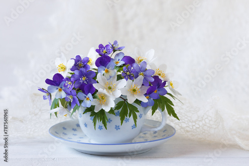 Bouquet of spring hepatica flowers, anemones, pansies, violets in a cup on a white wooden table, beautiful card