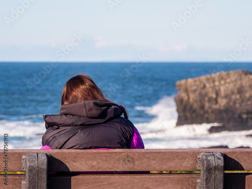 Teenager girl enjoy stunning nature of Kilkee coast and cliff, county Clare, Ireland. Rough coastline and blue cloudy sky. Travel and tourism. Irish landscape scene. Warm day. photo