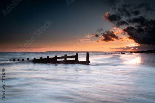 Long exposure landscape photograph at Camber sands beach on a warm evening, Image shows the beautiful sunset and glowing sky with a damaged wooden groyne subject and a receding tide photo