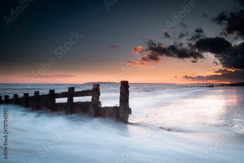 Long exposure landscape photograph at Camber sands beach on a warm evening, Image shows the beautiful sunset and glowing sky with a damaged wooden groyne subject and a receding tide