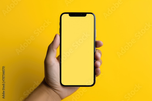 Man hand holding smartphone with blank yellow screen on yellow background. Mockup cell phone screen © vejaa