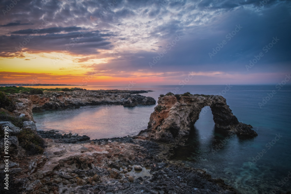 Rocky coastline with a natural arch at punta Asparano, near Siracusa. Sunrise time. June 2023
