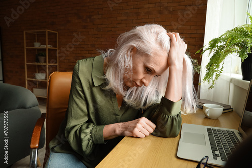 Depressed mature woman sitting near table at home photo