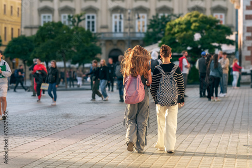 Urban socializing captured by two Gen Z friends walking through a historic town square among young people, reflecting the combination of modern living and timeless architecture