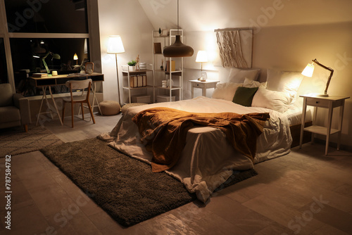 Interior of bedroom with workplace and glowing lamps at night photo