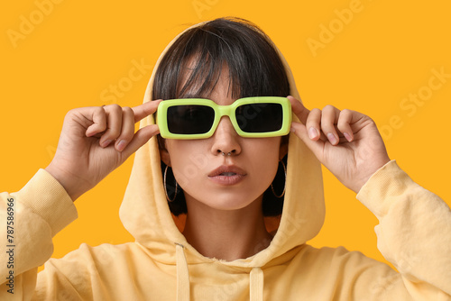 Stylish young woman in sunglasses with nose piercing on yellow background © Pixel-Shot