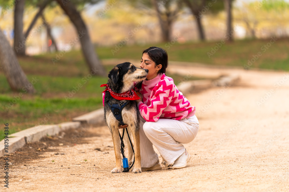 A heartwarming scene of a woman affectionately kissing her dog, seated on a serene park pathway A heartwarming scene of a woman affectionately kissing her dog, seated on a serene park pathway
