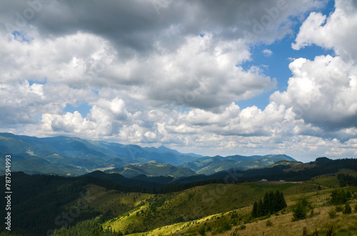 Scenic view of lush green mountains with small wooden shepherds house In the distance under a sky filled with fluffy clouds. Carpathian Mountains, Ukraine 