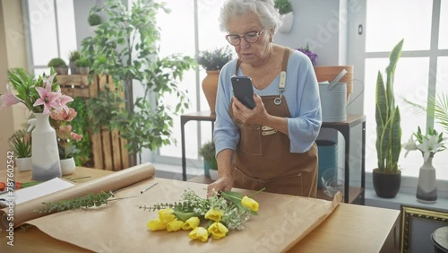 Senior woman using smartphone in flower shop surrounded by plants and blooms photo