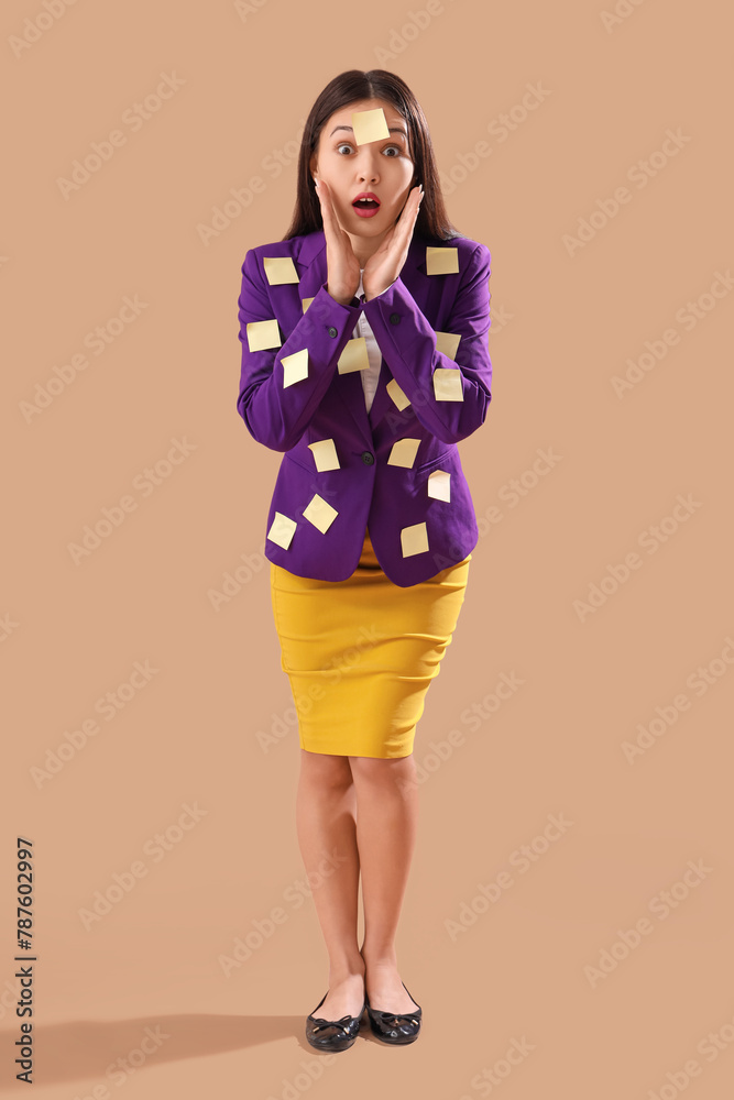 Funny shocked Asian businesswoman with sticky notes on brown background