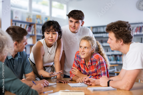 Positive teenage students working and discussing in groups in college library