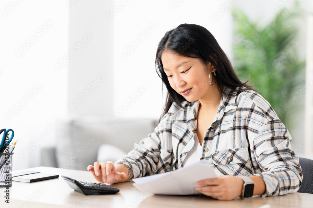 Young chinese woman preparing home budget using calculator sitting in the living room Young chinese woman preparing home budget using calculator sitting in the living room