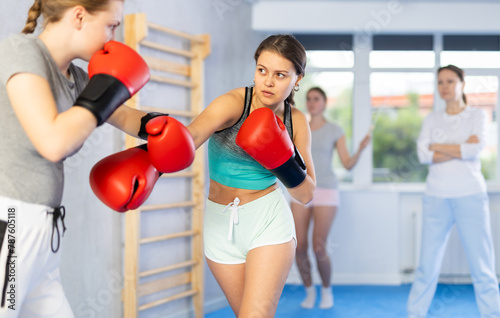 Young female co-participant and woman sparring partners during training battle fight using technique of boxing match under supervision of woman instructor. Boxing section for women, sport as lifestyle