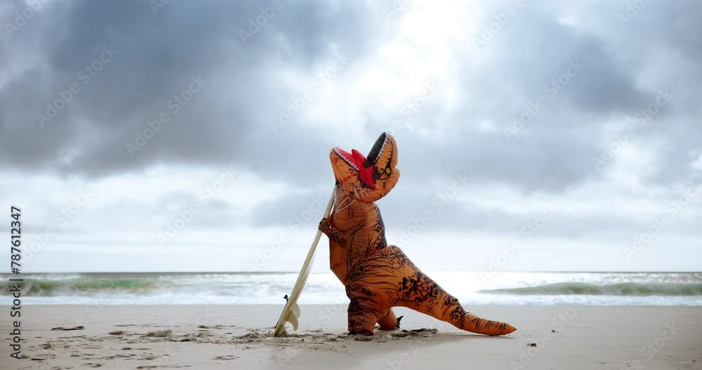 Beach, surfboard and person in dinosaur costume on sand outdoor by ocean or sea for struggle. Comic, sports and travel with adult surfer in t rex outfit for surfing holiday or vacation in nature