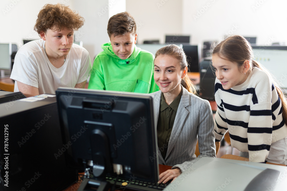 Female teacher and her students, young girl and boys, looking at monitor of PC during computer science lesson.