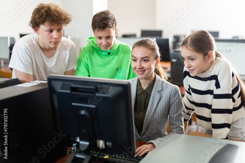 Female teacher and her students, young girl and boys, looking at monitor of PC during computer science lesson. © JackF