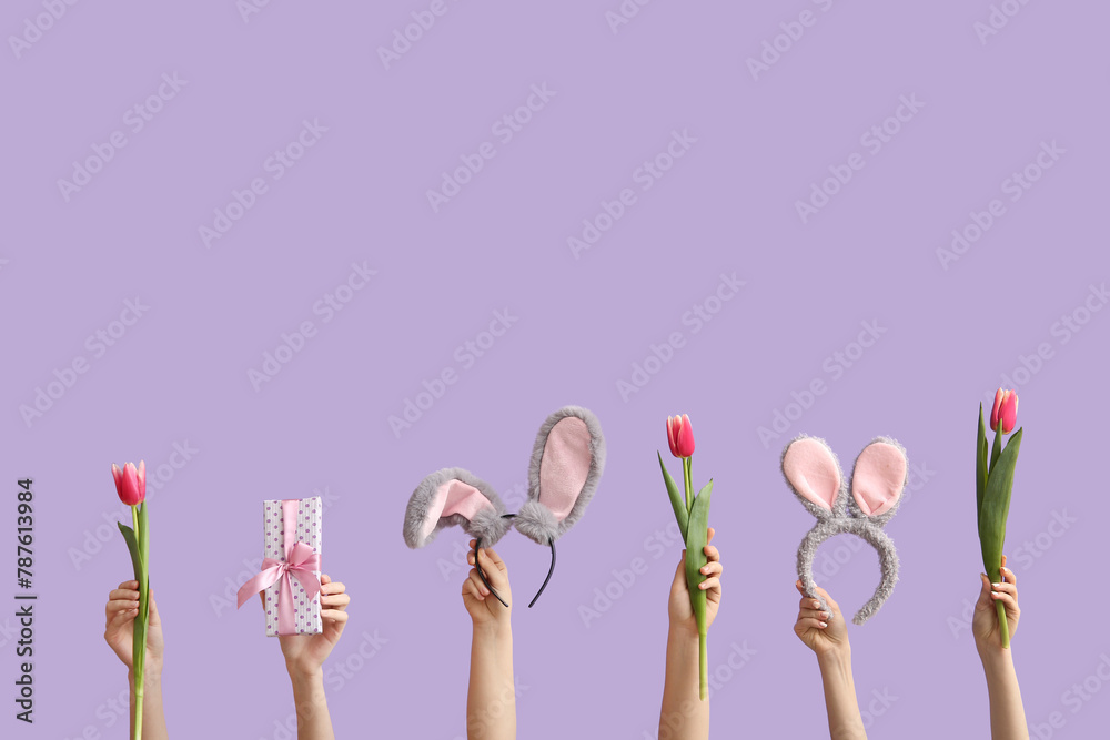 Female hands with tulips, gift and bunny ears headbands on violet background. Easter concept.