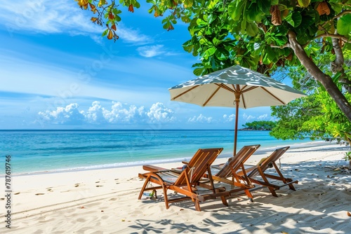 Wooden sun loungers under a parasol on a pristine beach, flanked by palm fronds and a view of the tranquil sea. © vachom
