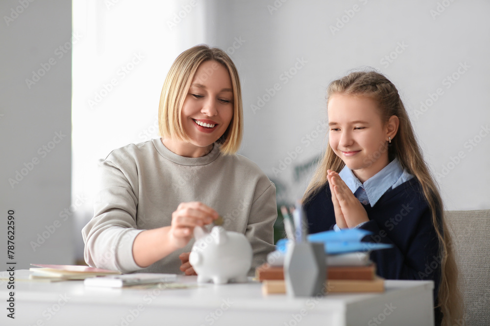 Mother with her daughter putting coin into piggy bank at home. Education savings concept Mother with her daughter putting coin into piggy bank at home. Education savings concept