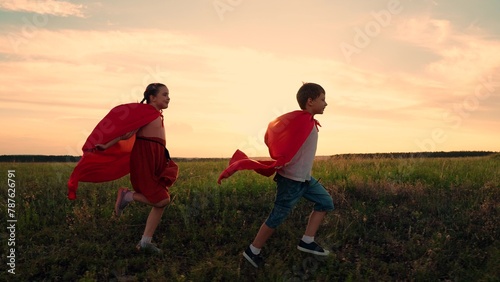 Superhero child. Boy girls in red cloak, Child dreams of becoming superhero. Happy girls, boy kids play superheroes they run across green field in red cloak. Children games dreams. Slow motion.