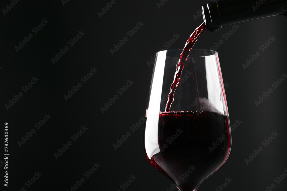 Obraz premium Pouring red wine into glass against black background, closeup. Space for text